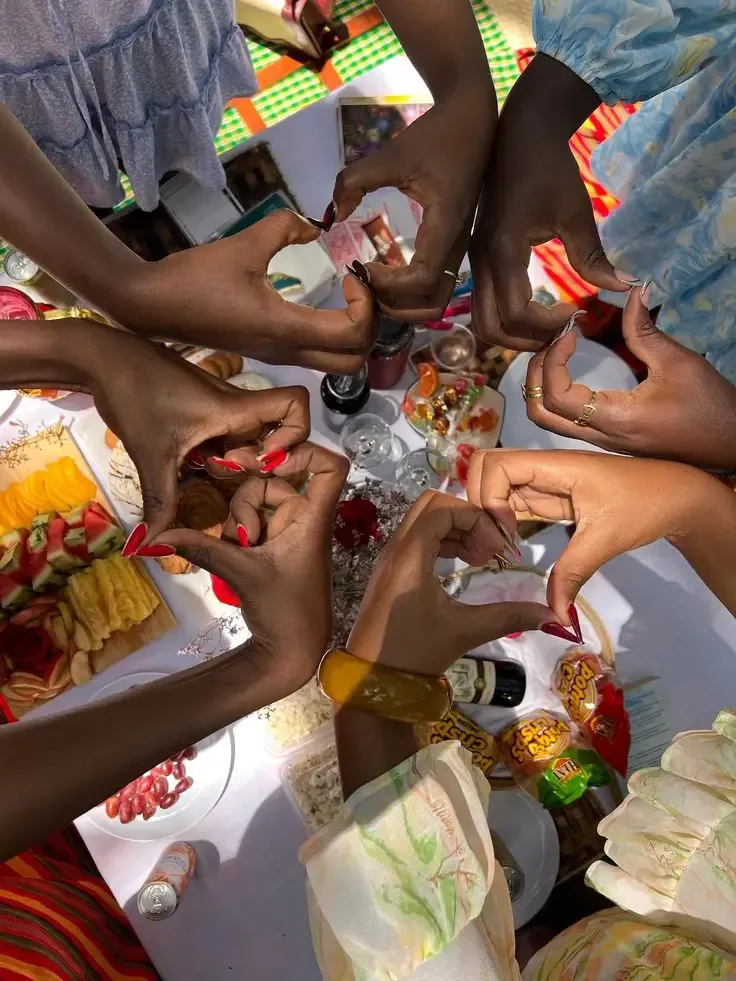 New friends joining hands into heart shapes over a picnic table full of snacks