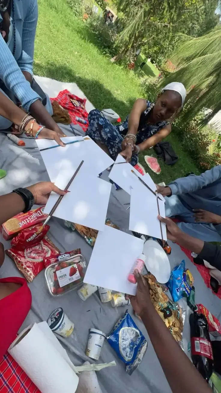 Friends sitting on a picnic blanket playing a game with paper and paintbrushes
