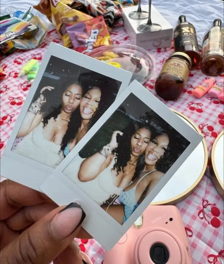 Two friends holding up instant printed photos of themselves at a picnic
