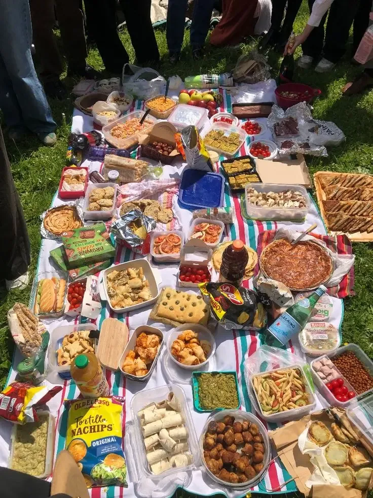 A picnic blanket covered in shared snacks, baked treats and drinks