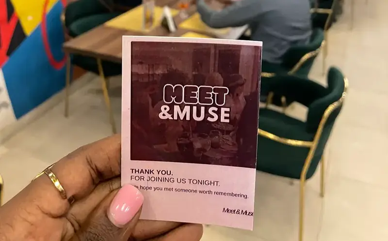 A Meet & Muse thank-you card held up at a dinner